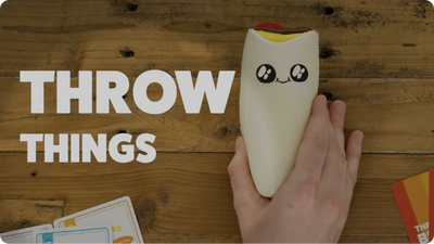 Hand holding a plush avocado above the words throw things 